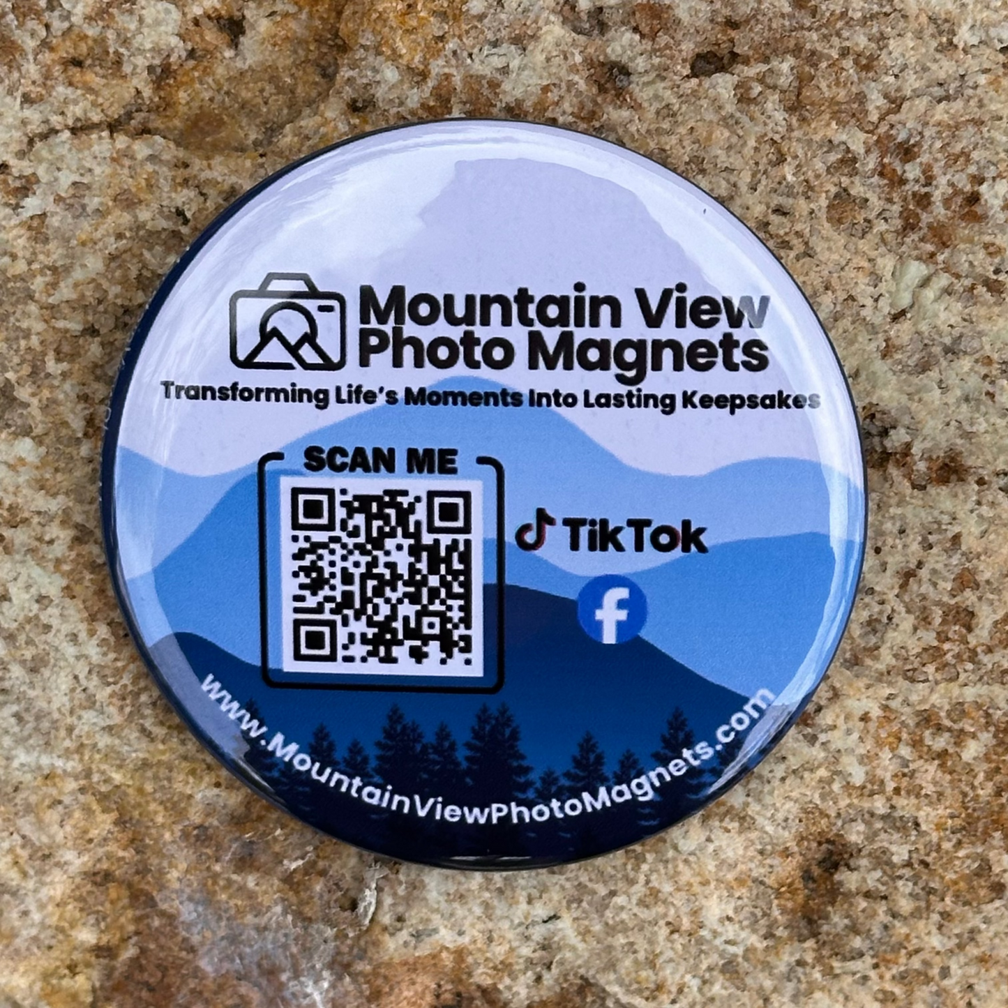 Round promotional pinned back button with QR code and social media information on a rock surface.