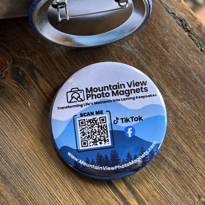 Round promotional pinned back button with QR code and social media information on a wooden surface.